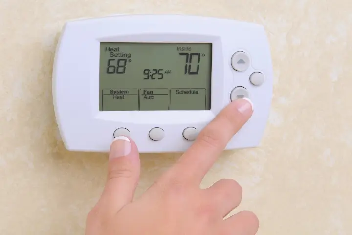 Hand adjusting thermostat to increase temperature to keep warm with help of TAP insulation installed in the home